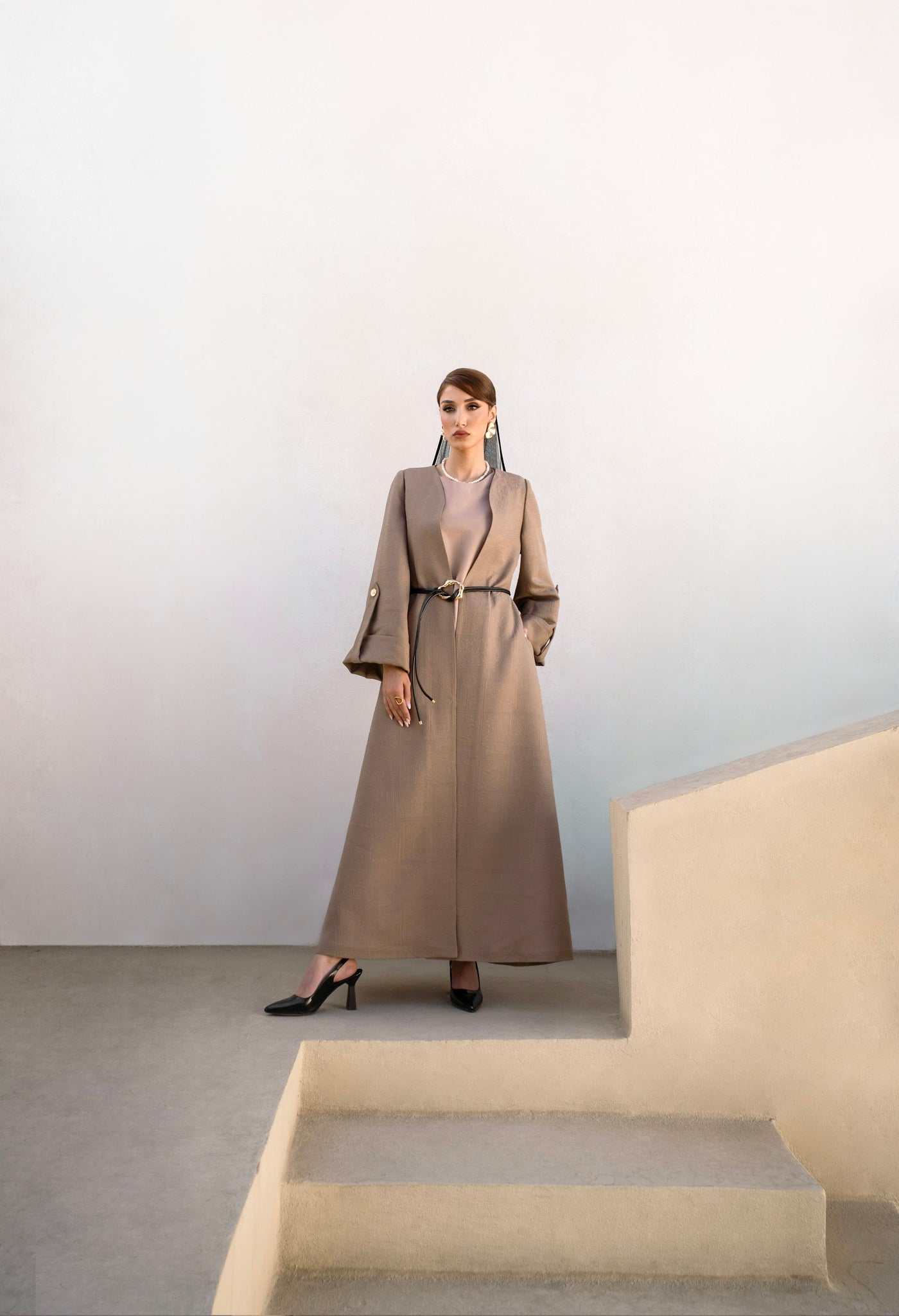 Longue silhouette en manteau beige dans un escalier de pierre